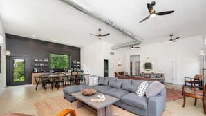 Amplia sala de estar con un sofá seccional gris, una mesa de centro de madera y un comedor con un ventanal grande.
