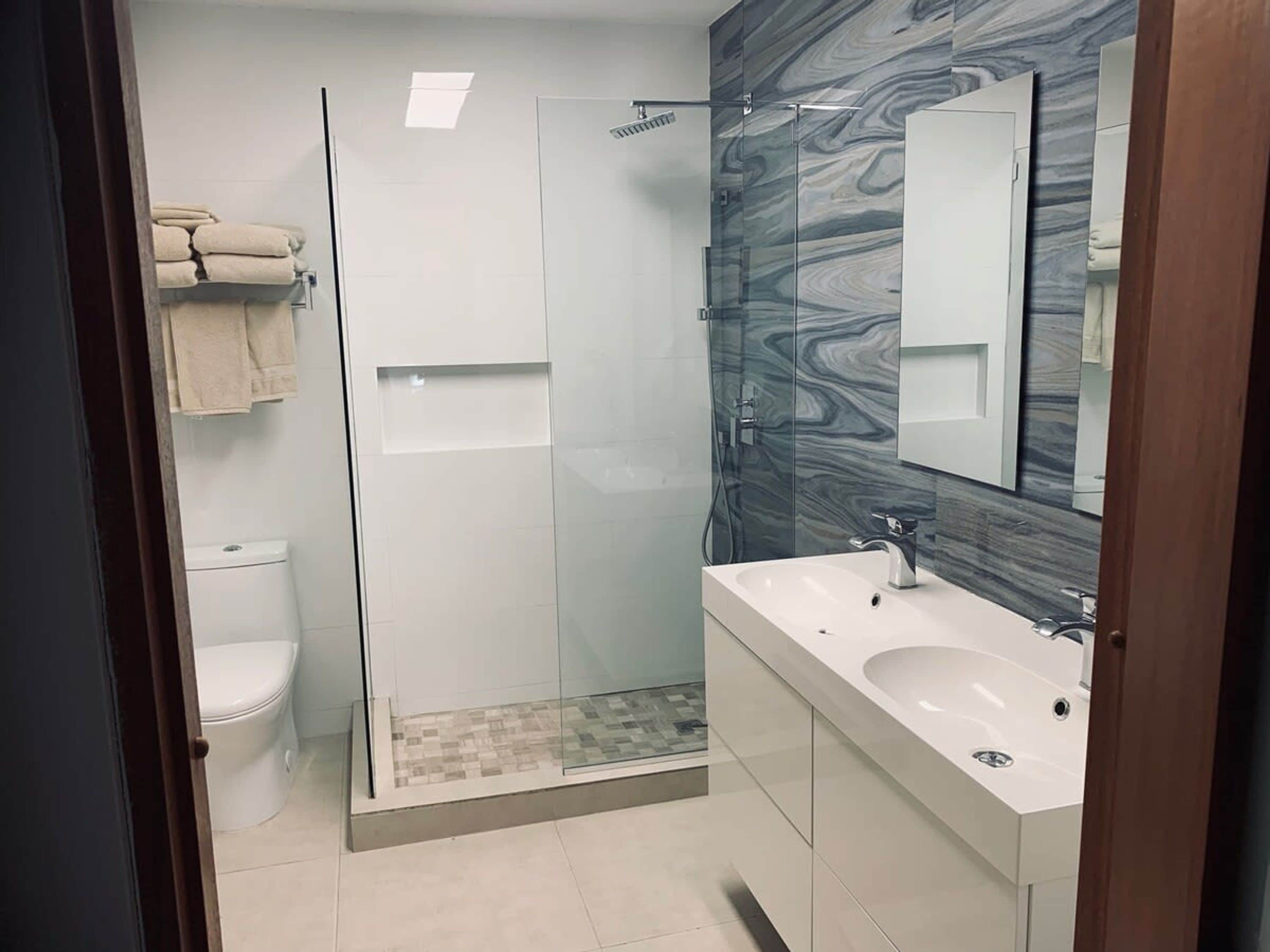 A modern bathroom with a glass-enclosed shower, a white toilet, and a vanity with two sinks.