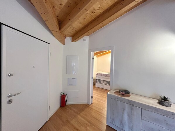 Un pasillo con techo de madera, una puerta blanca, un extintor y una cama al fondo.