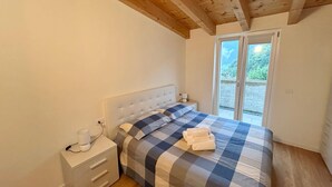 Ein Schlafzimmer mit Bett, Nachttisch, Schubladeneinheit und Fenster mit Blick ins Grüne.