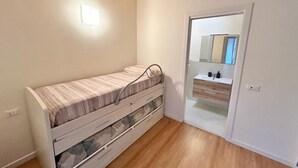 Ein kleines Zimmer mit einem Einzelbett, Holzboden, einem Nachttisch und einem Spiegel über dem Waschbecken.