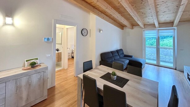 Ein moderner Wohnraum mit Holzboden, einer Essecke mit Tisch und Stühlen, einer Couch und Blick durch eine Glastür.