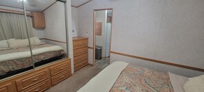 A bedroom with a bed, a dresser, a mirror, and a door leading to a bathroom. - 2-BR Getaway w/ HUGE screened porch, Golf Cart, Pool, & Boat Ramp near Wolf Bay (Elberta)