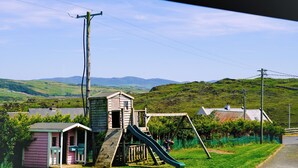 A playground with a slide and climbing structure, surrounded by green fields and hills.