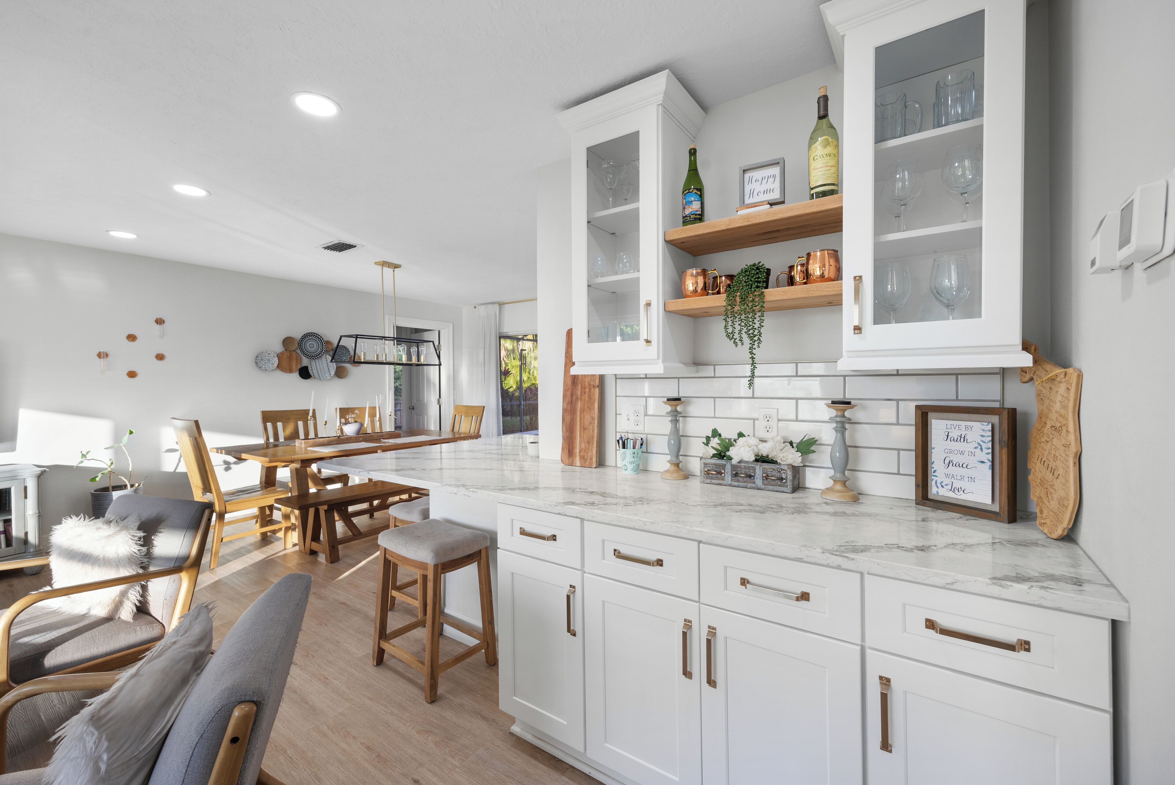 A modern kitchen with white cabinetry, marble countertops, and wooden dining chairs.