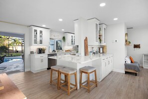 A modern kitchen with white cabinetry, a large island with stools, and a view of a backyard.