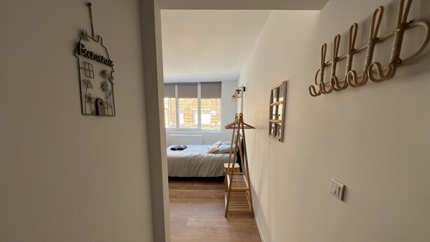 Un passadís condueix a una habitació amb un llit, un sòl de fusta i una finestra.