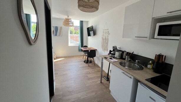 A modern kitchen with a microwave, sink, and a compact refrigerator. There is a dining area with a table and chairs, and a large mirror on the wall. - Le Boheme, studio 2p (Lens)