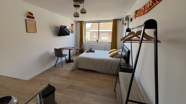 A compact room with a bed, a desk, a chair, a TV, and a window with curtains. - Le studio Sang & Or, 2p (Lens)