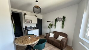 A compact living space with a dining table, a sofa, a kitchen area, and a window. - Le Jardin Botanique : Balnéo 2p (Lens)