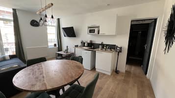 Un espace de vie compact comprenant un coin repas, une kitchenette et un téléviseur fixé au mur.