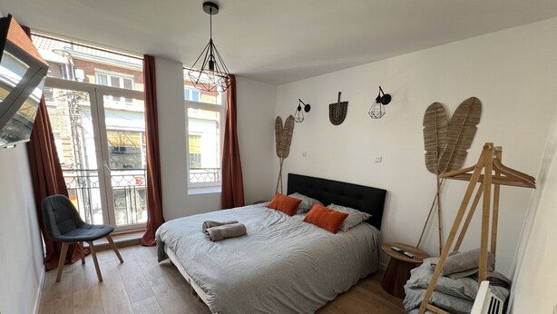 A bedroom with a bed, a chair, a radiator, and a window with curtains.
