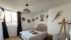 Un dormitorio con cama, lámpara colgante, ventana con cortinas y decoración en la pared.