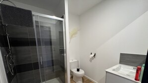 Un baño moderno con ducha de vidrio, inodoro y lavamanos con espejo.