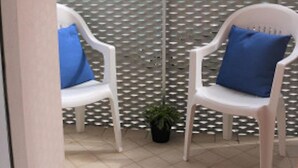 Ein Balkon mit zwei weißen Plastikstühlen, jeder mit einem blauen Kissen, und einem Blumentopf.