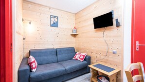 A wooden cabin room with a blue sofa, a small wooden table, and a TV mounted on the wall.