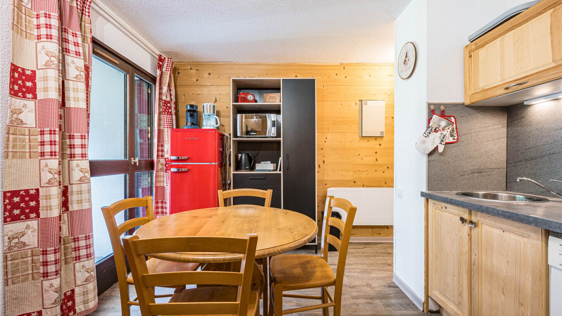 Cocina compacta con una mesa y sillas de madera, un refrigerador rojo y un microondas.