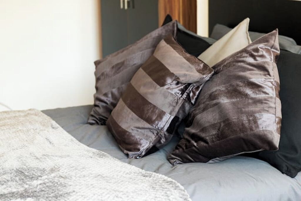 A bed with grey bedding and multiple pillows, including a striped one.