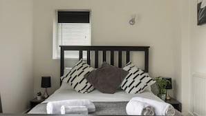 A neatly made bed with striped pillows, a bedside lamp, and a small potted plant on a nightstand. - The Old Sawmill - Entire apartment - Syston (Leicestershire)