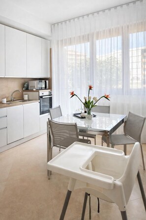 A modern kitchen with white cabinets, a microwave, and a dining area with a glass table and chairs.