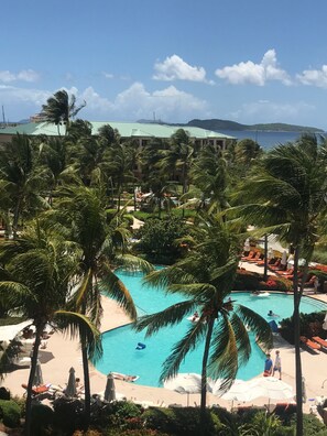 A resort pool area with palm trees, lounge chairs, and a view of the ocean. - Stunning three bedroom condo in beautiful St Thomas. The 3rd BR can be a king. (St Thomas)