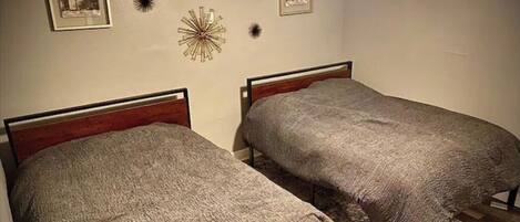 Two single beds with wooden headboards, a decorative wall piece, and framed pictures on the wall.