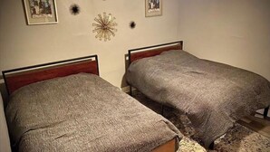 Two single beds with wooden headboards, a decorative wall piece, and framed pictures on the wall.
