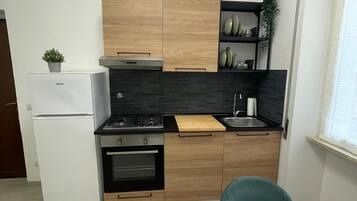 A compact kitchen with wooden cabinets, a white refrigerator, a stove, and a sink.