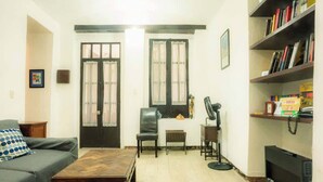 A living room with a sofa, a coffee table, a chair, a fireplace, a bookshelf, and a window with curtains. - Regina 70 · Amazing Historic Colonial Duplex by Cathedral (Mexico City)