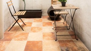 A small, enclosed patio area with a tiled floor, a wooden chair, a table with a potted plant, and a decorative wall-mounted light fixture. - Regina 70 · Amazing Historic Colonial Duplex by Cathedral (Mexico City)