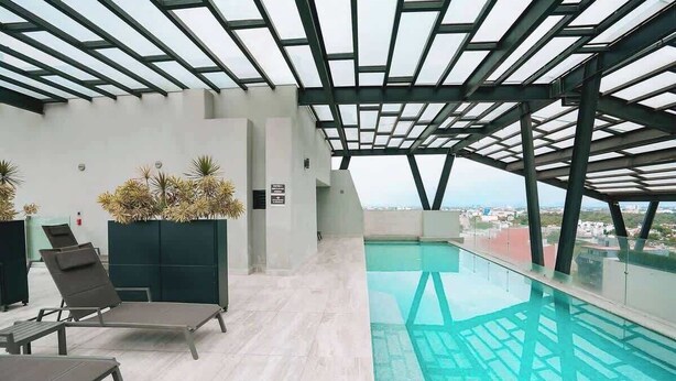 A modern indoor pool with a glass ceiling, lounge chairs, and a view of the city. - Rooftop Pool Oasis in Roma Norte w/ Gym & A/C (Mexico City)