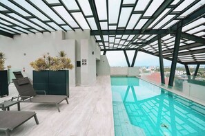 A modern indoor pool with a glass ceiling, lounge chairs, and a view of the city. - Rooftop Pool Oasis in Roma Norte w/ Gym & A/C (Mexico City)