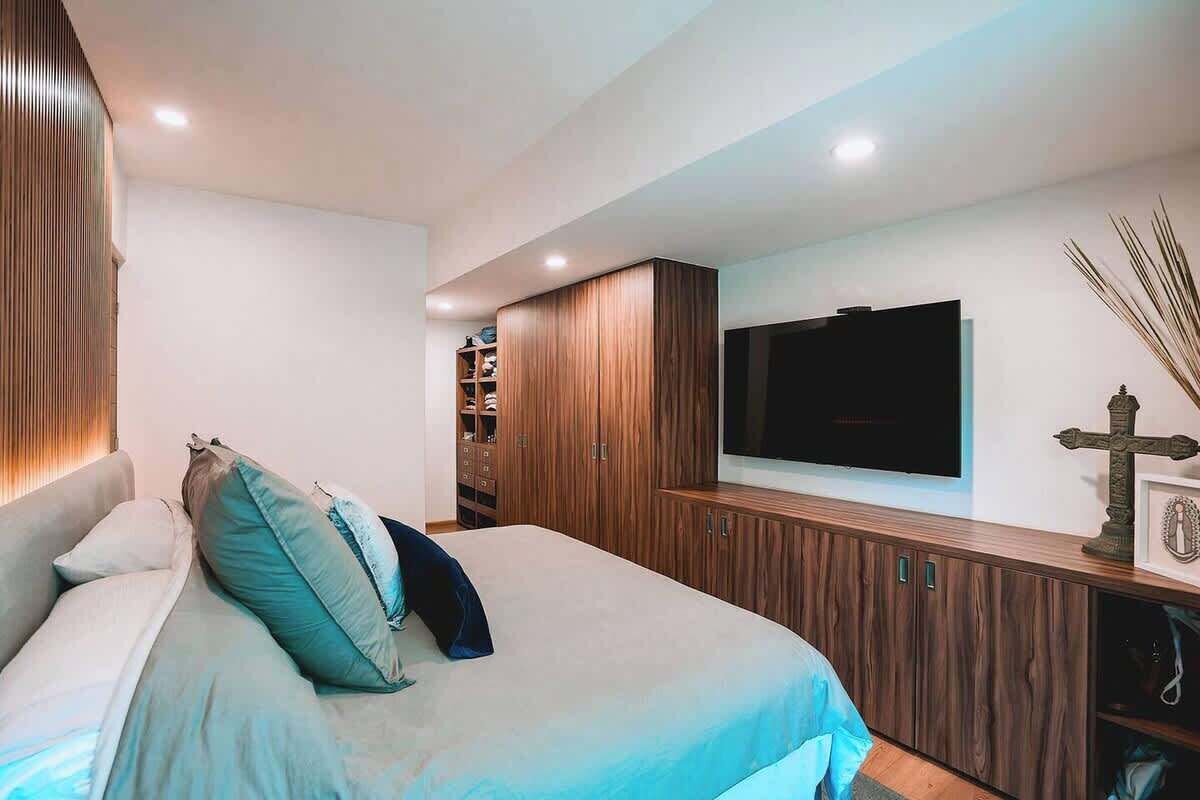Een slaapkamer met een bed, een houten garderobe, een ingebouwde televisie en een decoratief kruis.