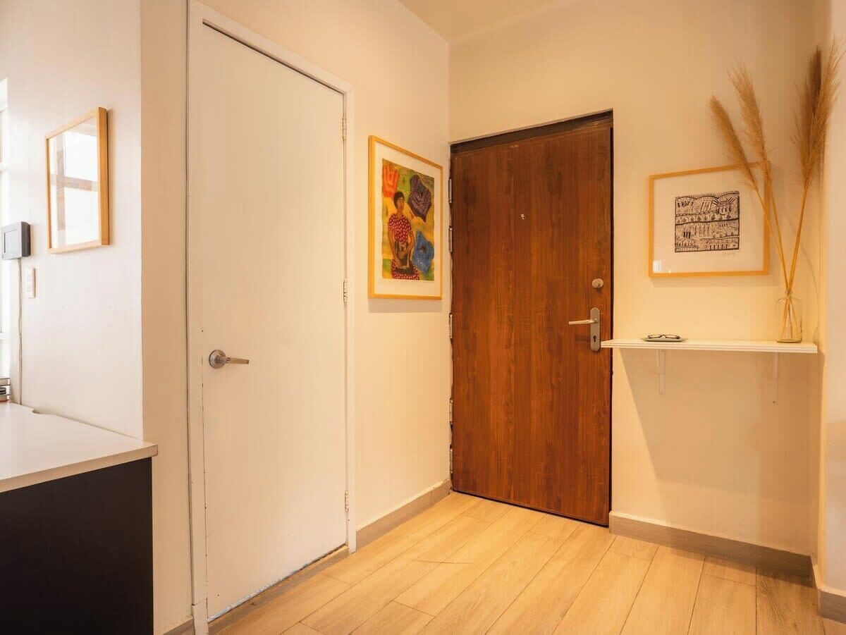 A hallway with a wooden door, a framed picture on the wall, and a shelf with a vase.