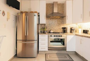 Une cuisine moderne dotée d’appareils électroménagers en acier inoxydable, de meubles blancs, de plans de travail en granit et d’un four encastré.