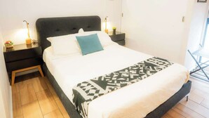 Un lit recouvert d’un couvre-lit à motifs, une table de chevet avec une lampe et un miroir accroché au mur.