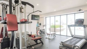 Une salle de sport équipée de matériel d’exercice, d’un tapis de course et dotée de grandes fenêtres.