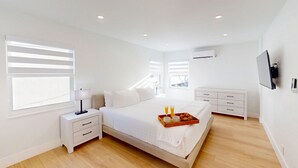 A modern bedroom with a large bed, bedside tables, a TV, and a tray of breakfast items. - Beach Condo King Bed Lush Patio w BBQ Birch Key Four (Fort Lauderdale)