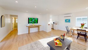 A modern living room with a wooden floor, a dining area with a table and chairs, a kitchen in the background, and a TV on a stand. - Beach Condo King Bed Lush Patio w BBQ Birch Key Four (Fort Lauderdale)