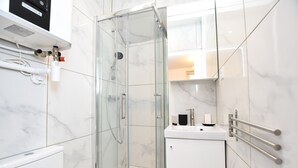 A modern bathroom with a glass-enclosed shower, white marble tiles, and a white sink with a towel rack.