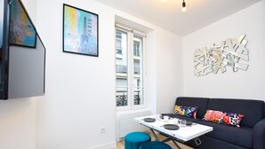 A modern living room with a black sofa, colorful cushions, a white table, and a large abstract art piece on the wall.