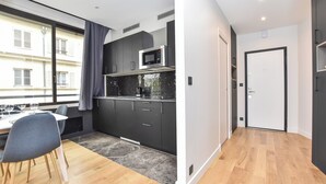 A modern kitchen with dark cabinets, a microwave, and a dining area with a table and chairs. - Chic Apartment - 1br/4p - Near Opera Garnier (Paris)