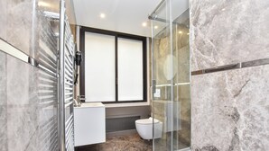 A modern bathroom with a glass shower enclosure, a white toilet, and a built-in sink with a window above. - Chic Apartment - 1br/4p - Near Opera Garnier (Paris)