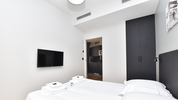 A modern hotel room with a bed, a flat-screen TV, and a wardrobe. - Chic Apartment - 1br/4p - Near Opera Garnier (Paris)