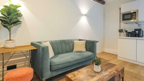 A modern living space with a teal sofa, a wooden coffee table, and a small orange ottoman. A potted plant adds greenery. - Relaxing Urban Getaway, Notre Dame (Paris)