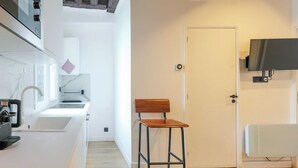 A modern kitchen with a built-in stove, a sink, and a countertop. There is a wooden stool and a white door in the room. - Relaxing Urban Getaway, Notre Dame (Paris)