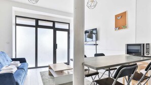 A modern living room with a sofa, a dining table with chairs, a flat-screen TV, and a kitchen area with a microwave. - Bright Apartment - 1br/4p - Bibliotheque Francois Mitterrand (Paris)