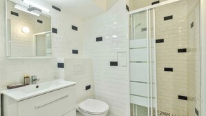 A modern bathroom with a white sink, toilet, and shower area, featuring a tiled wall with black accents. - Bright Apartment - 1br/4p - Bibliotheque Francois Mitterrand (Paris)