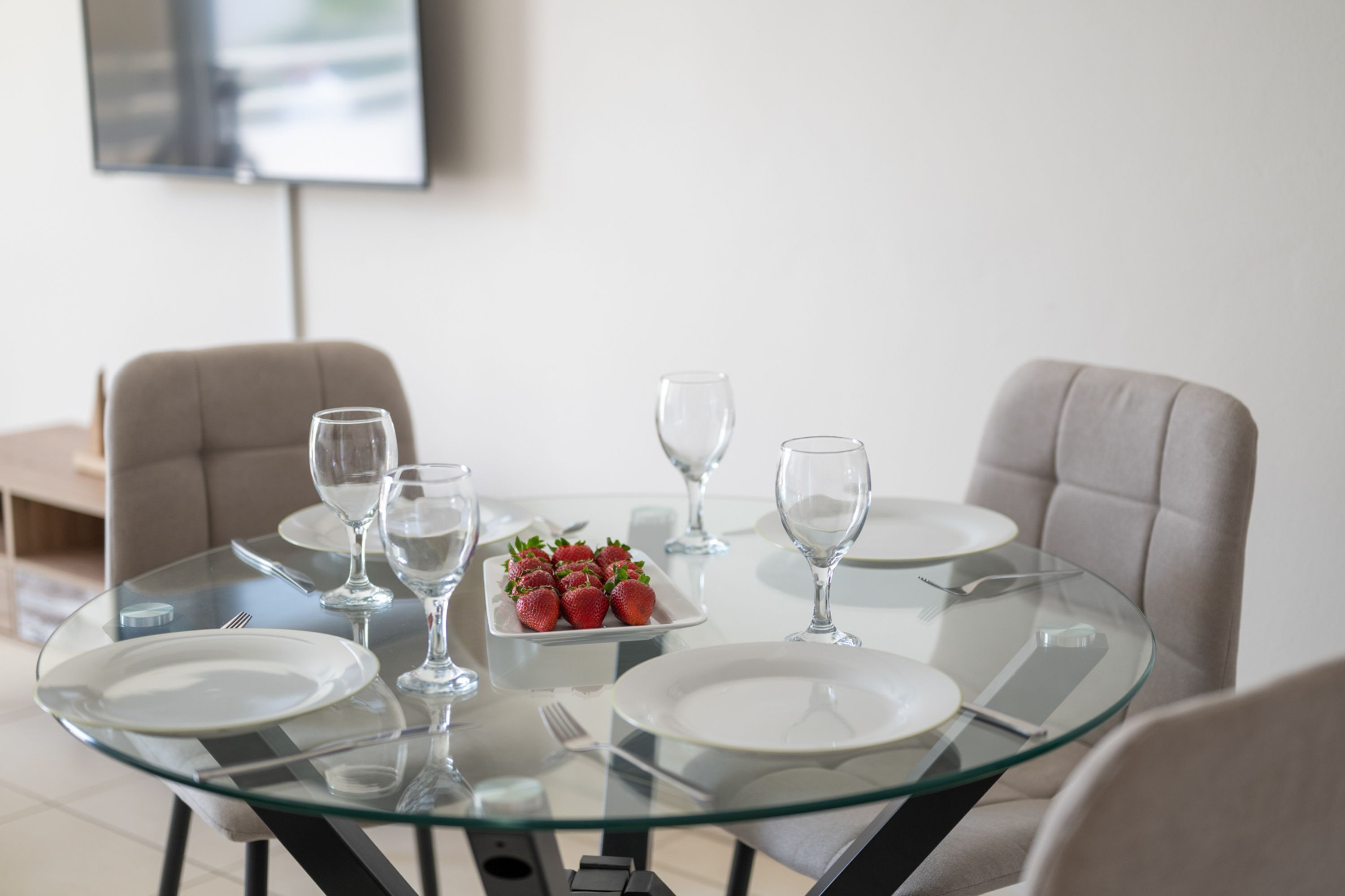 Una mesa de comedor con superficie de vidrio, rodeada de sillas, y un plato de fresas.