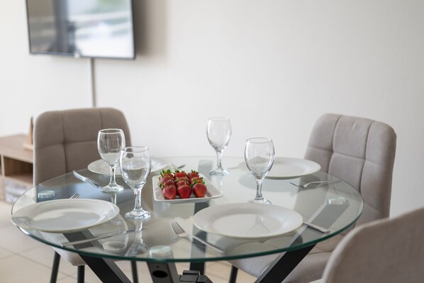 A dining table with glass top, surrounded by chairs, and a plate of strawberries. - Narcissos Nissi Beach Apartment C5 (Ayia Napa)